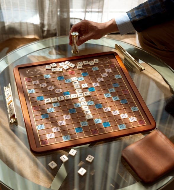 A close-up shot of a classic wooden Scrabble board game on a glass table, spelling out "TENNESSEAN".