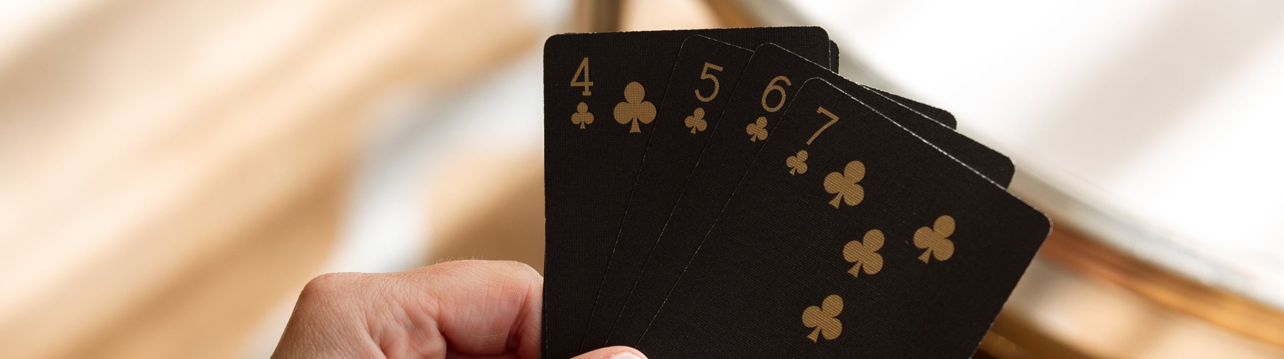 A close-up shot of hands holding five black playing cards with gold lettering at a reflective wooden table.