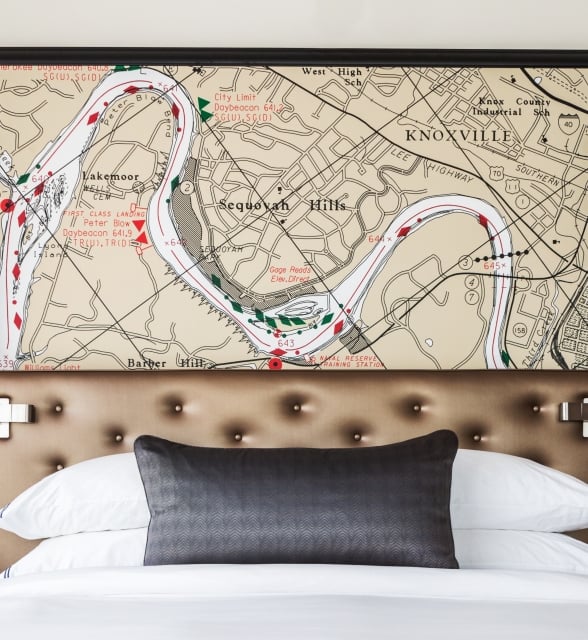 A framed map of "KNOXVILLE," featuring a winding river and areas like "Sequoyah Hills" and "Lakemoor," hangs above a bed with a tufted headboard and pillows.