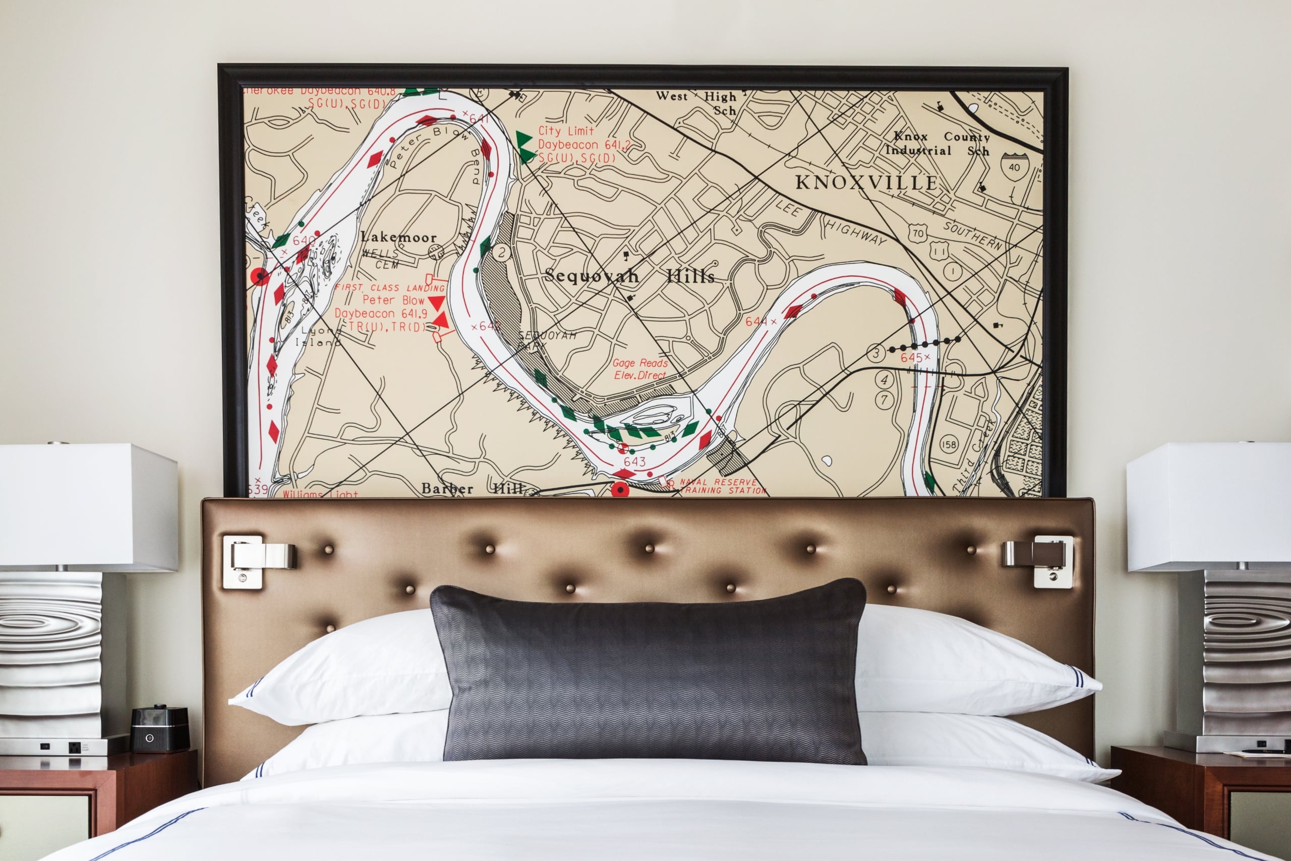 A framed map of "KNOXVILLE," featuring a winding river and areas like "Sequoyah Hills" and "Lakemoor," hangs above a bed with a tufted headboard and pillows.