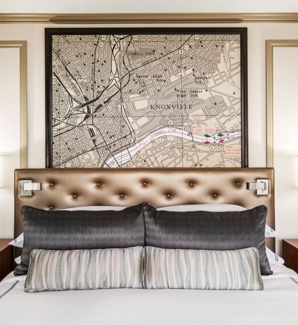 A bed is centered with a tufted headboard, dark and striped pillows. Above, a framed map depicts "KNOXVILLE", "UNIVERSITY OF TENNESSEE", "FORT SANDERS", "Adair Park", "Hampton Park". Modern lamps flank it on nightstands.
