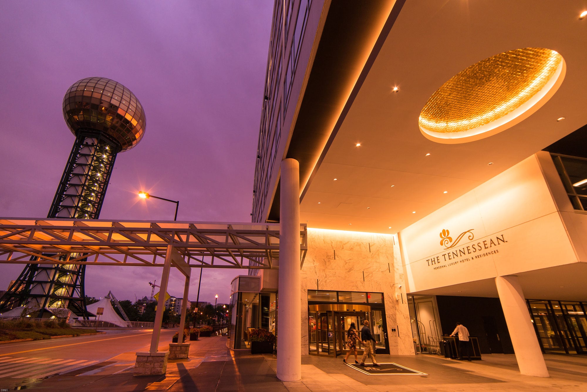 A golden sphere tower stands illuminated next to a modern hotel entrance glowing under a purple dusk sky, connected by a walkway. Sign reads: "THE TENNESSEAN. PERSONAL LUXURY HOTEL & RESIDENCES"