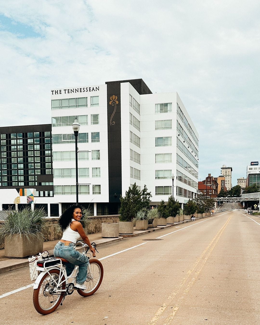 A woman smiles while riding a white bicycle on a street beside a white building reading "THE TENNESSEAN". Far right: "usbank".