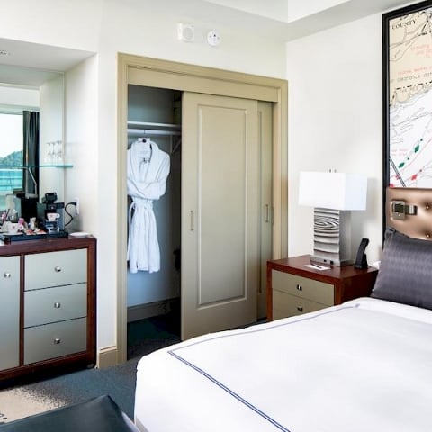 A hotel room features a white robe hanging in a partially open closet. A bed, dresser with coffee machine, and map artwork are also present. Text: COUNTY TRADING AREA clearance date