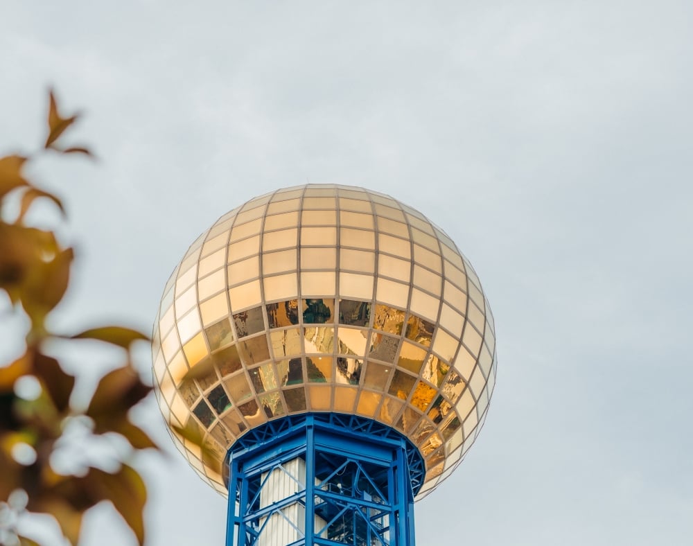 A close-up shot of the Sunsphere tower in Knoxville, featuring its iconic large glowing gold glass sphere against a pale sky.