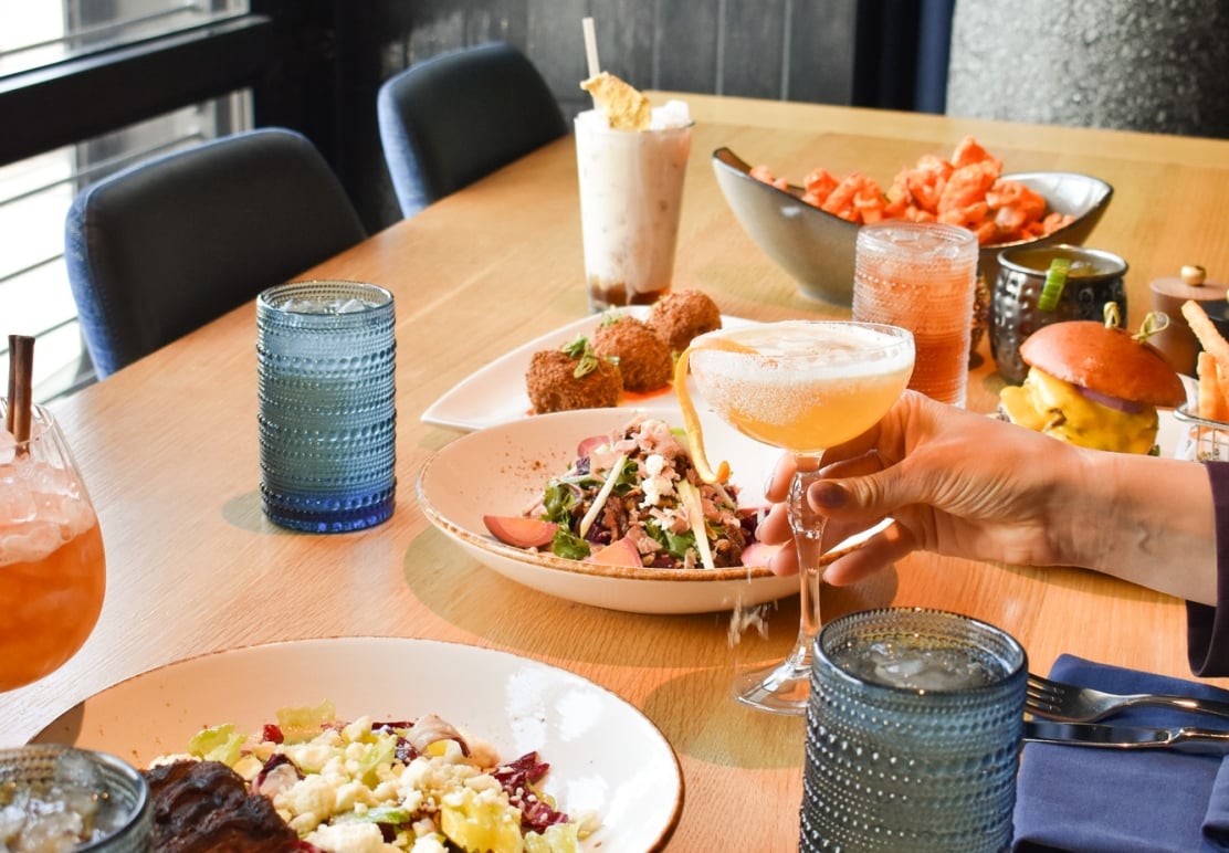 A close-up shot of a well-set restaurant dining table filled with colorful cocktails and various food plates.