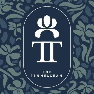 Dark blue oval emblem displays a white stylized floral symbol above a capital 'T' and "THE TENNESSEAN". It is set against a dark blue background with abstract blue and green floral patterns.